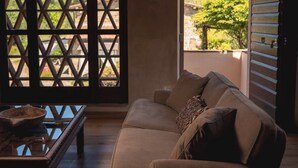 Une pièce avec un plancher en bois, un canapé marron avec des coussins, une table basse en verre et une fenêtre à croisillons.