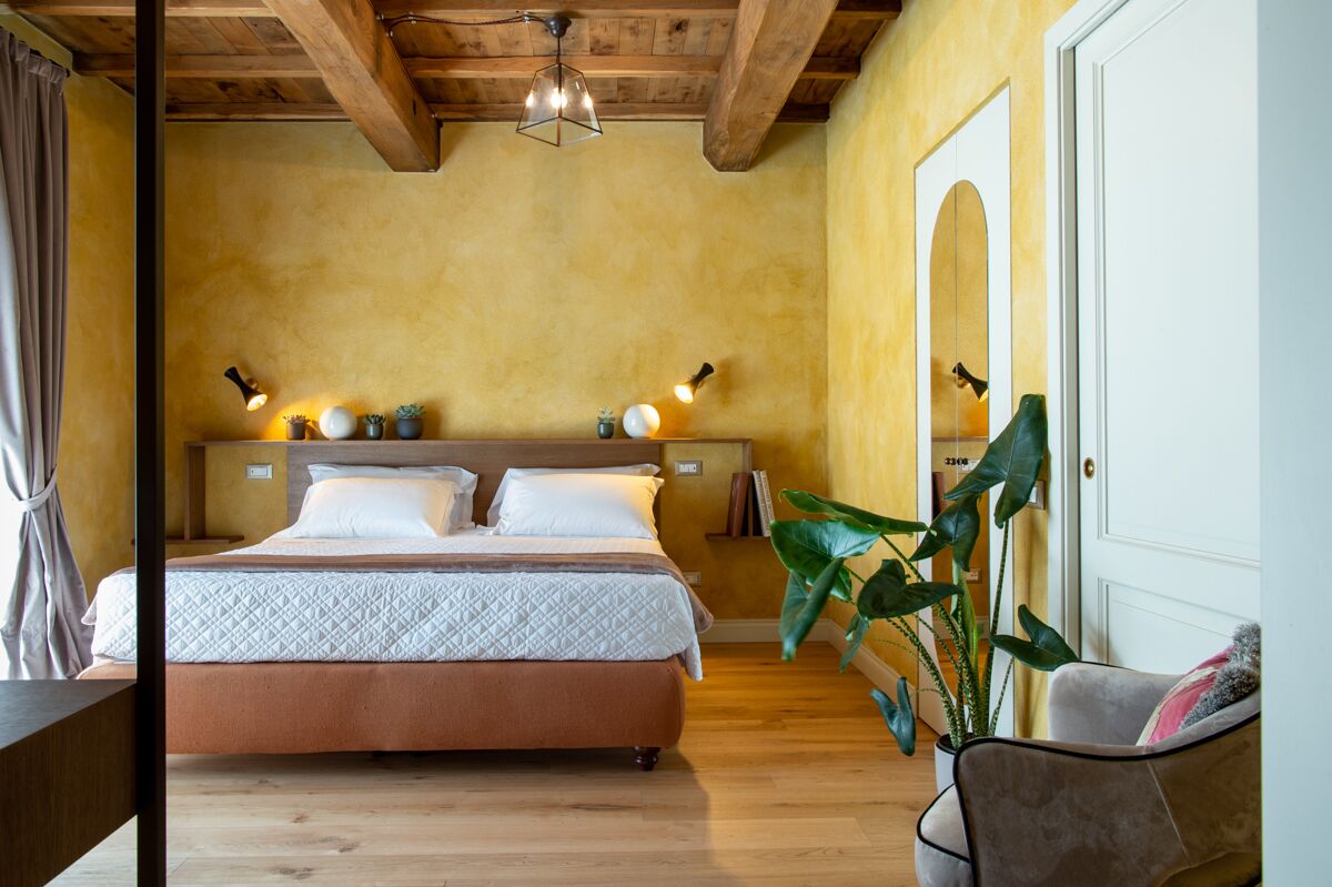 Un dormitorio con cama, lámparas de noche, una planta grande y techo de madera.