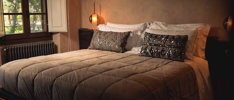 A bedroom with a large bed, a window, a radiator, and a wall-mounted light fixture.