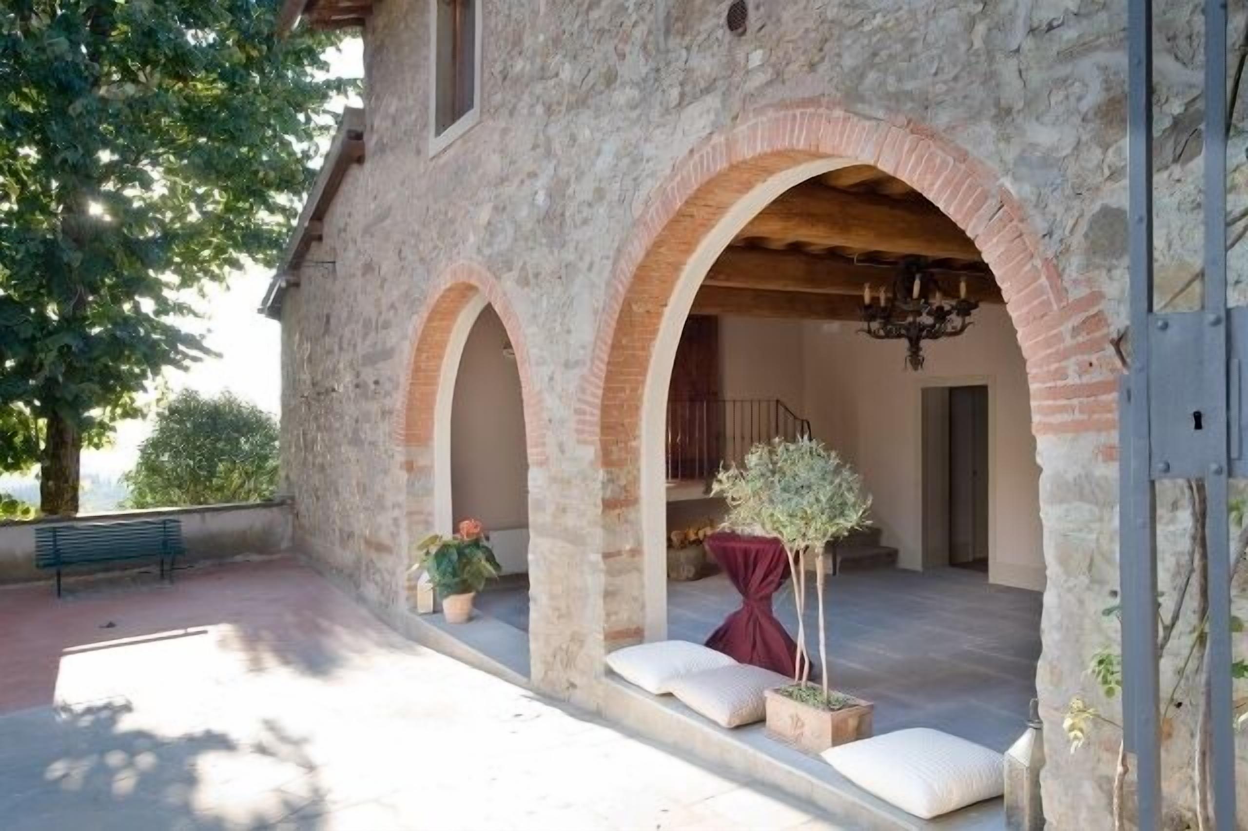 A stone building with arched doorways and a covered patio area with seating and potted plants.