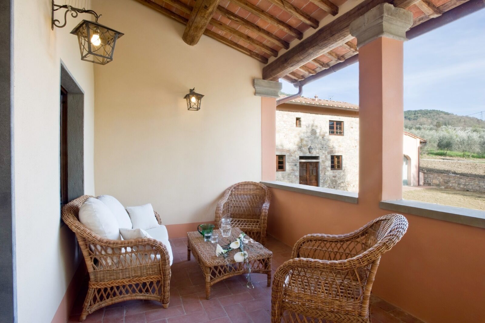 A balcony with wicker furniture, a table with glasses, and a view of a stone building.