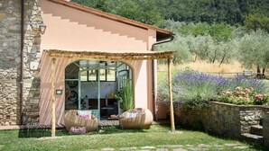 Un bâtiment en pierre doté d’un patio couvert, de sièges en plein air et offrant une vue sur une colline boisée.
