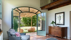 Une pièce dotée d’une porte en verre incurvée donnant sur un jardin, d’un meuble en bois et d’un tableau encadré accroché au mur.