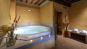Une salle de bain avec une grande baignoire, un vase en verre contenant des fleurs séchées et un banc avec des serviettes.