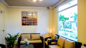 Ein Zimmer mit einer Couch, einem Couchtisch, einer Topfpflanze und einem Fenster mit Blick auf die Straße.