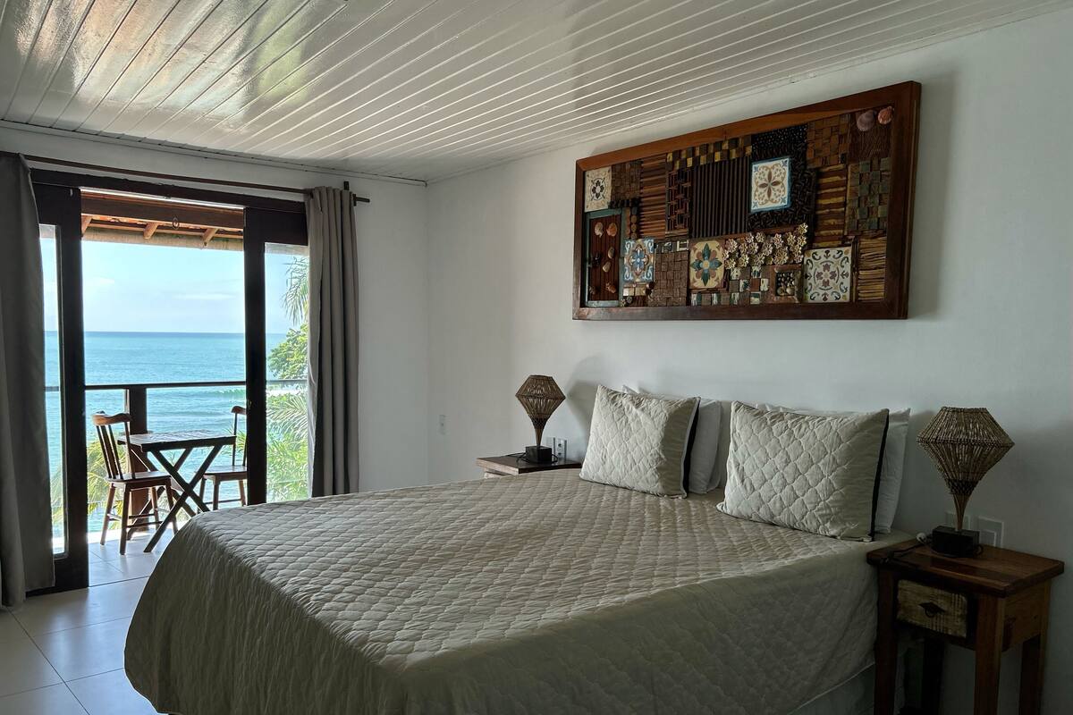 Un dormitorio con una cama grande, cabecera de madera, un adorno en la pared y vista al océano a través de una puerta corrediza.