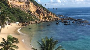 Un paisaje costero con una playa arenosa, un litoral rocoso y un acantilado con vegetación.