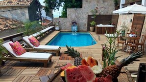 Un área junto a la piscina con sillones reclinables, una mesa de comedor y un frutero.