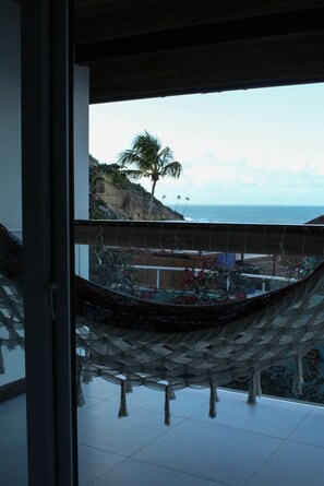 Uma rede numa varanda com vista para a costa, uma palmeira e o oceano.