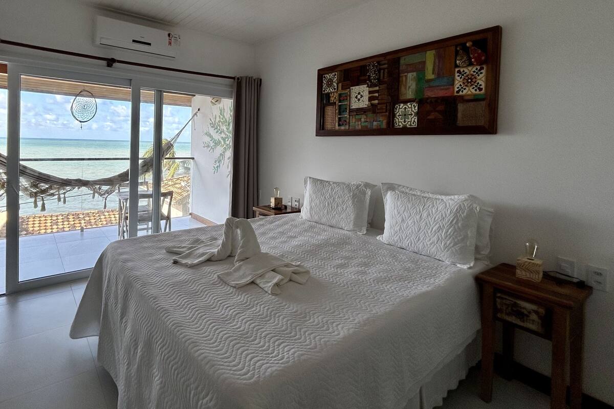 Un dormitorio con una cama grande, vistas al océano a través de una puerta corredera, una hamaca afuera y una pared decorada con azulejos.