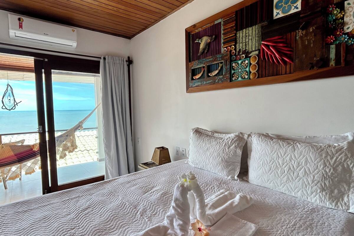 Habitación de hotel con una cama grande, techo de madera, vista a la playa y un panel decorativo en la pared.