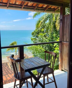 A wooden table and chairs on a balcony with a view of the ocean and palm trees. - Aroeira Eco Pousada (Cairu)