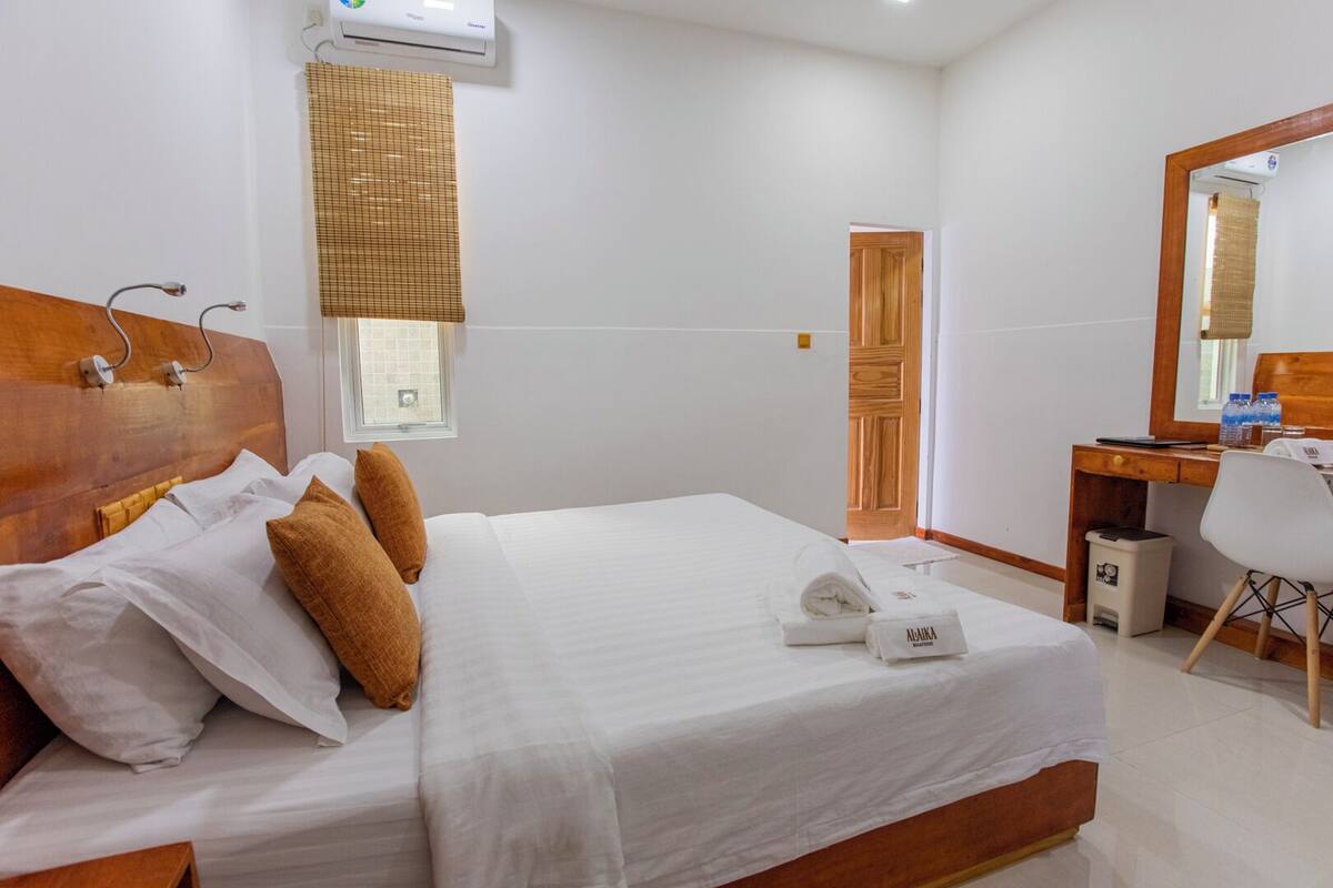 Una habitación de hotel con una cama grande, un cabecero de madera, un escritorio con una silla, un espejo y una ventana con persiana.