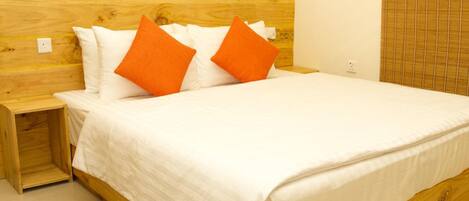 Una cama con ropa de cama blanca y dos almohadas naranjas, un cabecero de madera y una mesita de noche de madera.