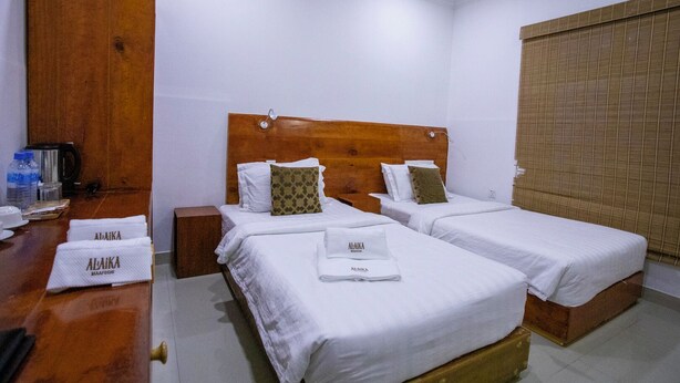 Habitación de hotel con dos camas individuales, un cabecero de madera, un escritorio de madera con una tetera y una ventana con persiana.