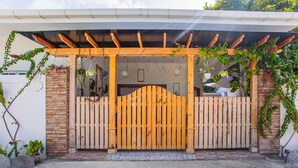 Una puerta de madera con un porche de madera encima, que da a una casa con un muro de piedra y un porche cubierto.