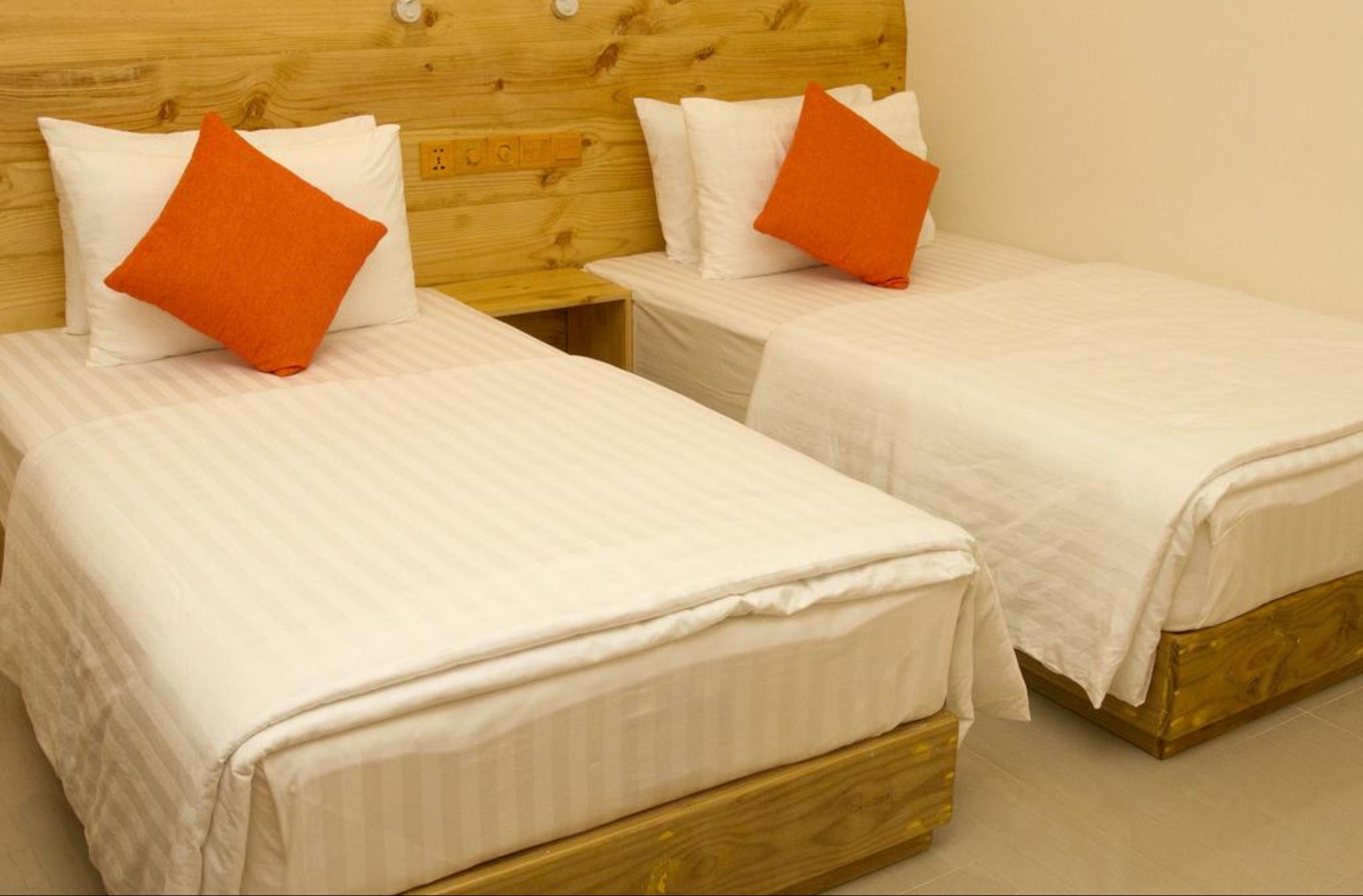 Two single beds with wooden headboards and white bedding, each with an orange pillow.
