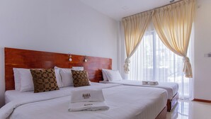 Une chambre d’hôtel avec une tête de lit en bois, deux lits, du linge de lit blanc, des coussins à motifs et une fenêtre avec des rideaux légers.