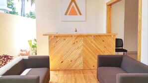 Un área de recepción con un mostrador de madera con patrón de espiga, dos sofás grises y un logotipo enmarcado en la pared.