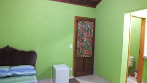 Une pièce comprenant un lit, un petit appareil électroménager blanc et une porte ornée de rideaux à motifs floraux.