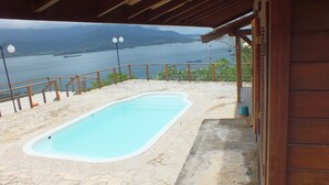 Une piscine avec une terrasse en pierre, une pergola en bois et une vue sur une vaste étendue d’eau et des montagnes.