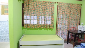 Quarto com cama, mesa com micro-ondas e cortinas florais.