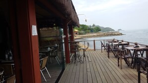 Un espacio de comedor al aire libre con mesas y sillas, una terraza de madera y vistas al mar.
