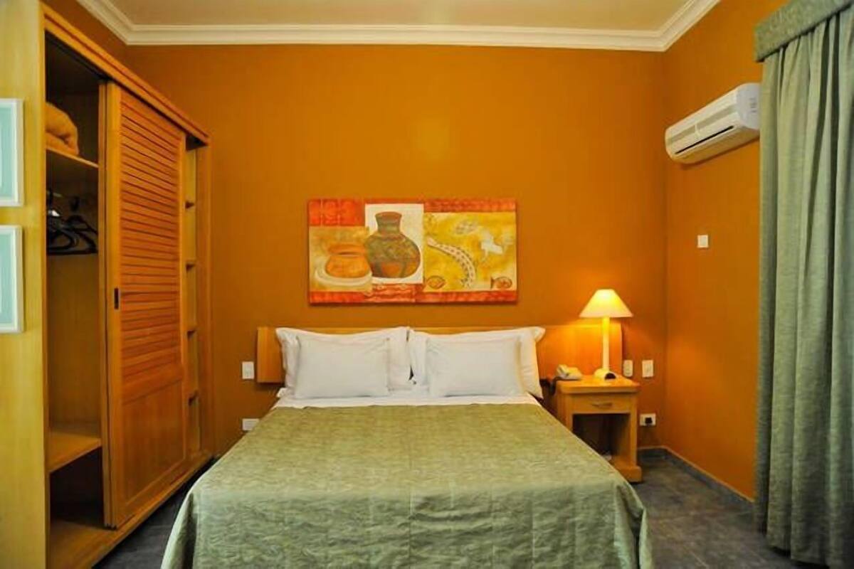 Una habitación de hotel con cama, mesita de noche, lámpara, aire acondicionado y armario.