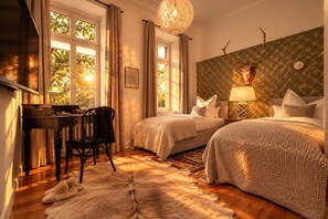 Ein Schlafzimmer mit zwei Betten, einem Schreibtisch, einem Stuhl, einer Lampe und einer Dekoration mit einem Hirschschädel an der Wand.