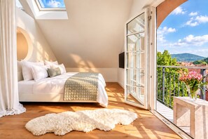 Ein Schlafzimmer mit Bett, großem Fenster und Balkon mit Blick auf Grünflächen und Berge.