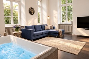 Un salon moderne avec un canapé d’angle, une grande fenêtre, un téléviseur à écran plat et un jacuzzi.