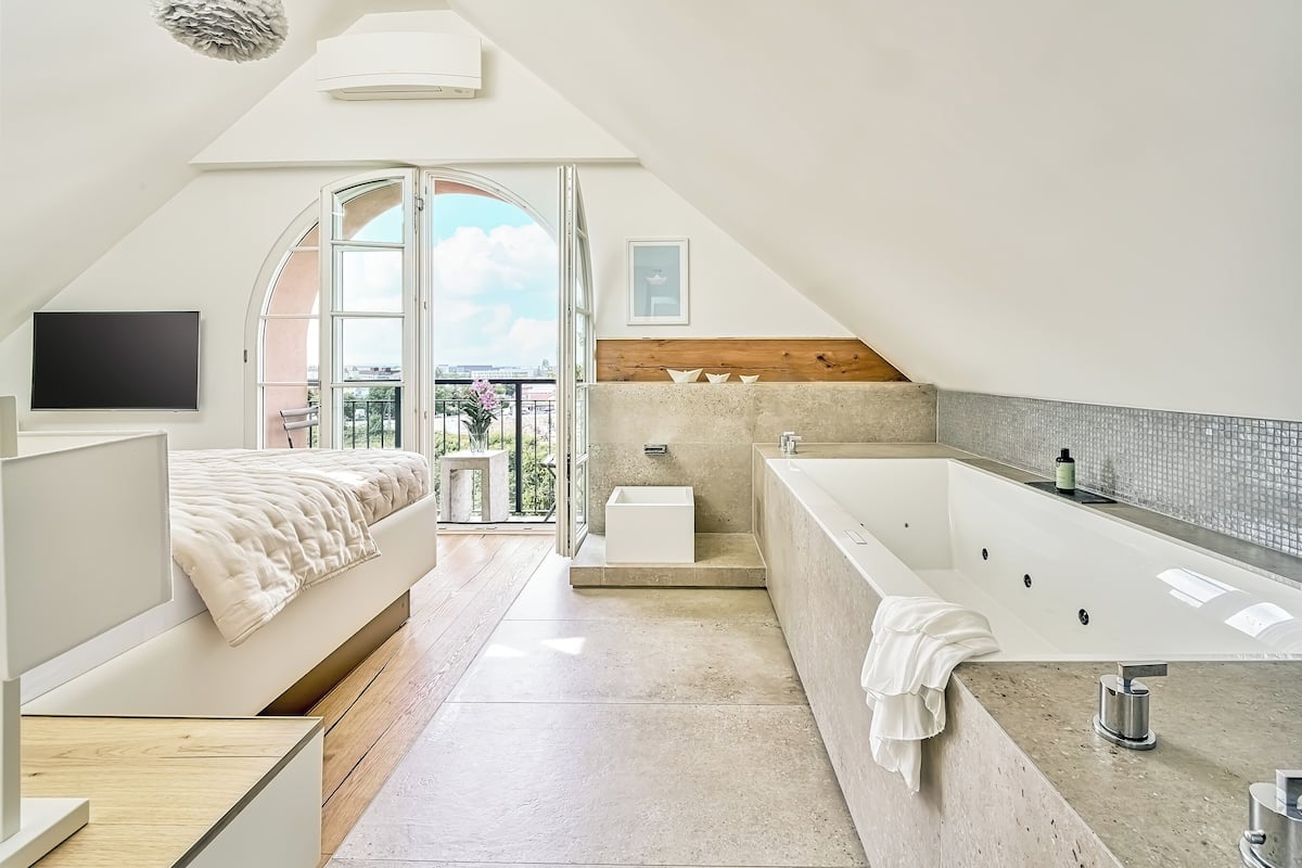 Ein modernes Schlafzimmer mit einem großen Bett, einem fest eingebauten Fernseher und einem Balkon mit Blick.
