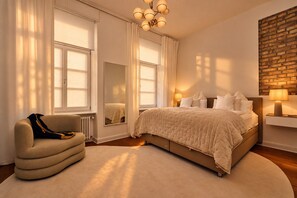 Une chambre avec un grand lit, une chaise, un miroir et un mur en briques.