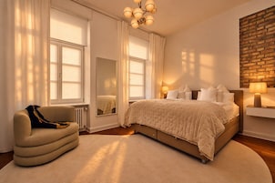 Een slaapkamer met een groot bed, een stoel, een spiegel en een bakstenen muur.