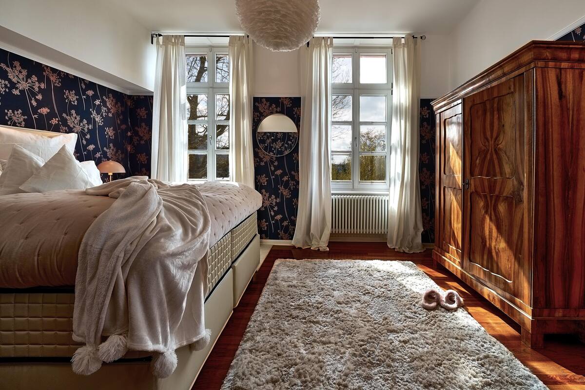 Ein Schlafzimmer mit einem Bett, einem großen Holzschrank, einem flauschigen Teppich und einem Fenster mit Vorhängen.