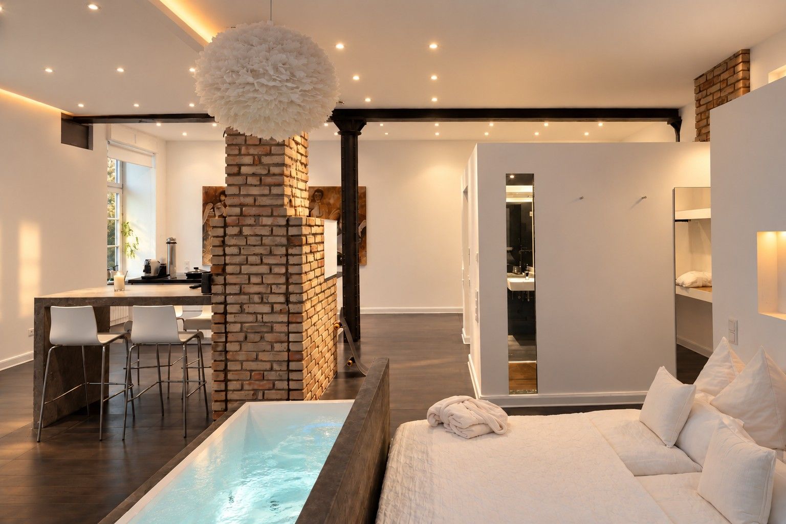 A modern hotel room with a large bed, a sitting area with a table and chairs, a brick fireplace, and a small pool.