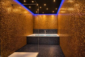 Une salle de bain moderne avec une grande baignoire, des murs recouverts de mosaïques et un luminaire au plafond.
