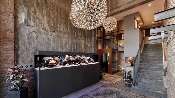 A reception area with a large aquarium, a staircase, and a modern chandelier. - Boutique Suites and Residences Heidelberg – Alte Zigarrenmanufaktur (Heidelberg)