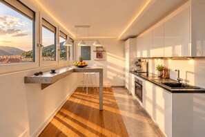 A modern kitchen with a bar area, large windows, and a view of the countryside. - Boutique Suites and Residences Heidelberg – Alte Zigarrenmanufaktur (Heidelberg)