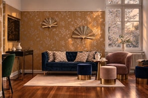Une pièce avec un canapé bleu foncé, un fauteuil rose, une table ronde et un mur décoratif orné de motifs floraux.