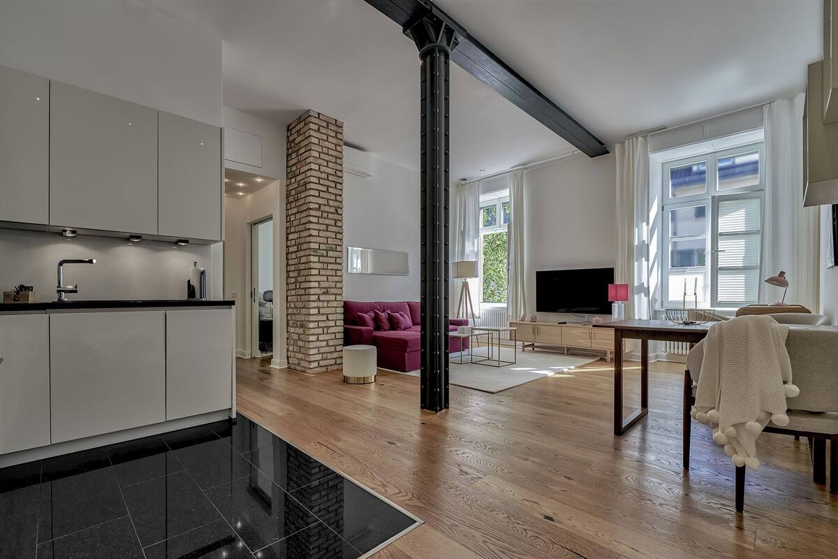 Eine moderne Küche mit weißen Schränken, einer schwarzen Arbeitsplatte und einem Kamin aus Backsteinen.
