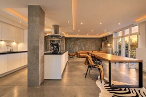 Eine moderne Küche mit integrierter Espressomaschine, einem Essbereich mit Holztisch und -stühlen sowie einem großen Fenster mit Blick ins Freie.