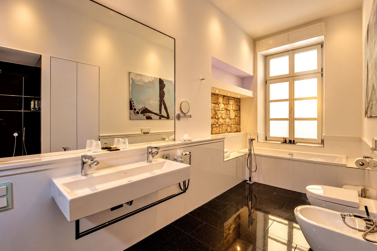 A modern bathroom with a large mirror, two sinks, a bathtub, and a toilet.
