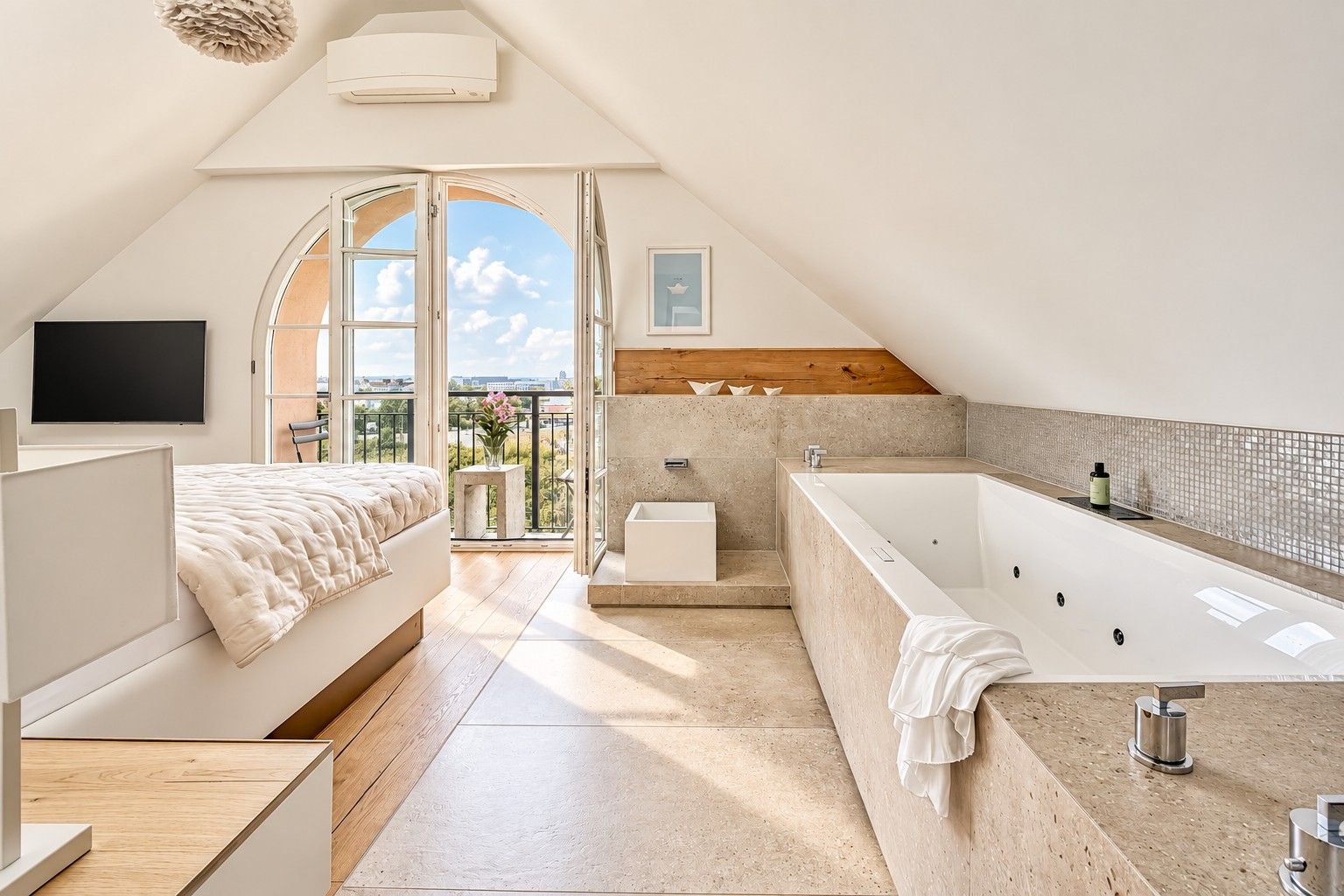 A modern bedroom with a large bed, a separate bathroom with a bathtub, and a balcony with a view.