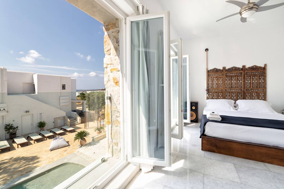 A bedroom with a bed, a ceiling fan, and a view of a pool and outdoor seating area.