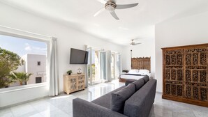 A modern living room with a grey sofa, a wooden cabinet, and a television. - Villa Pela (Paros)