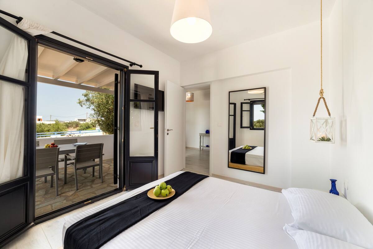 A hotel room with a bed, a black bedside table, a mirror, and a view of the outside balcony.