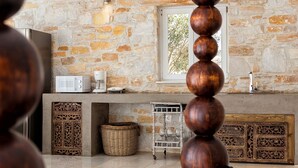 A kitchen with a stone wall, a microwave, a coffee maker, and a wicker basket. - Villa Pela (Paros)