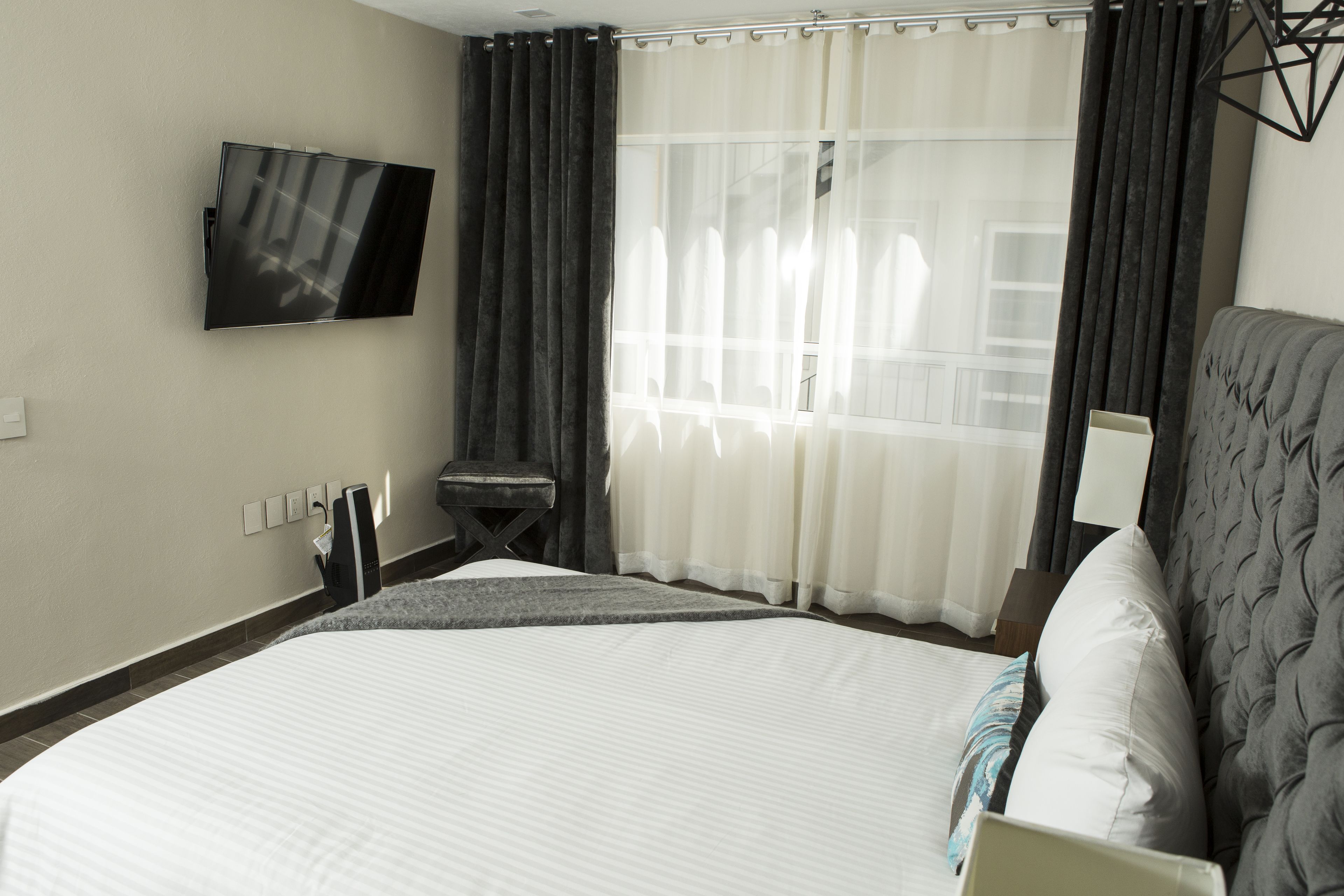 Une chambre d’hôtel dotée d’un grand lit, d’un téléviseur à écran plat fixé au mur, d’un petit coin salon et d’une fenêtre avec des rideaux.