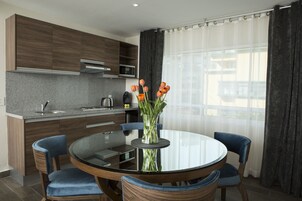 Une cuisine moderne avec des meubles de couleur bois foncé, un plan de travail en granit et une table ronde en verre, accompagnée de chaises.